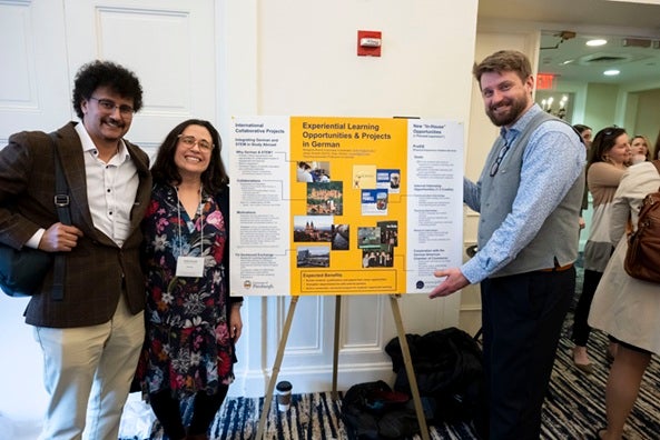 Three conference attendees stand next to a display sitting on an easel about Experiential Learning.