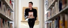 Professor Alaina Roberts Smiling woman sits on a chair between stacks of books