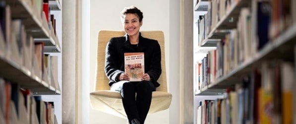 Smiling woman sits on a chair between stacks of books